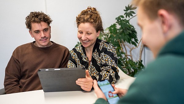 Drei Personen tauschen sich über Arbeitsmaterialien aus.