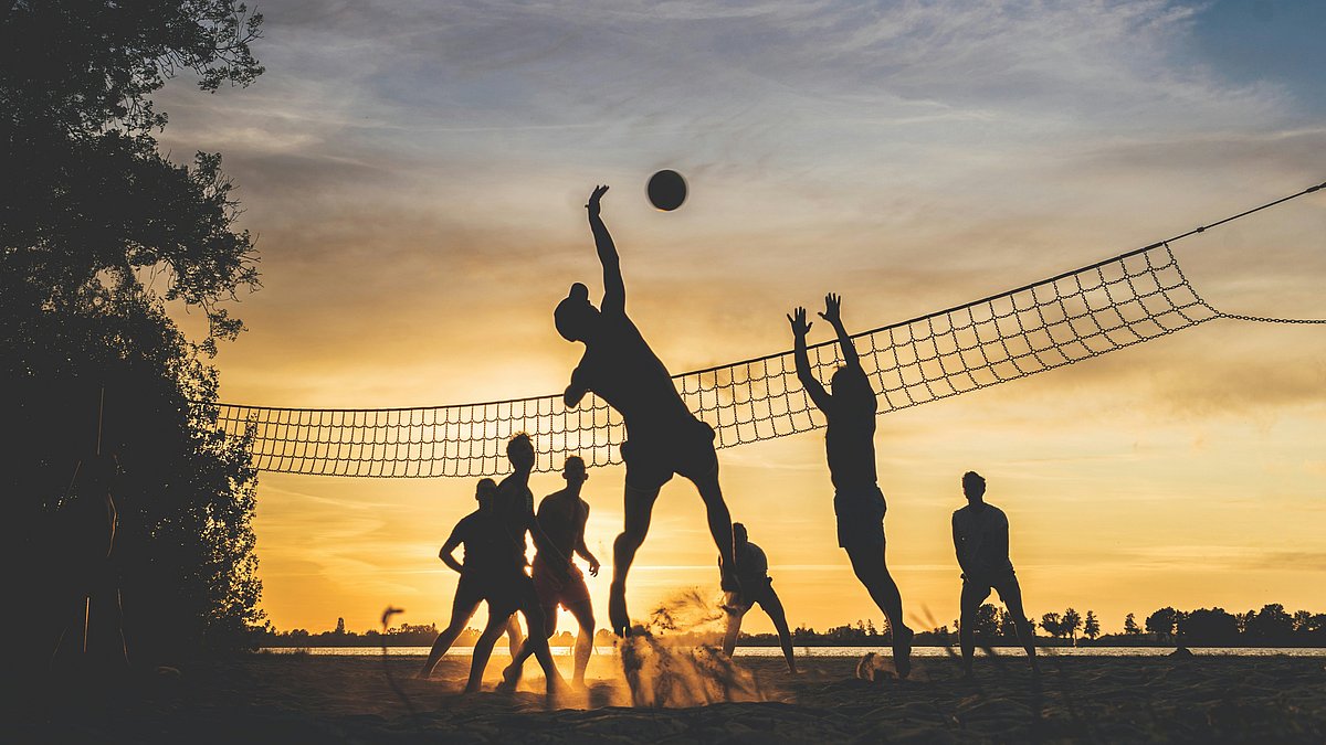 Junge Menschen spielen im warmen Licht des Sonnenuntergangs gemeinsam Volleyball im Freien.