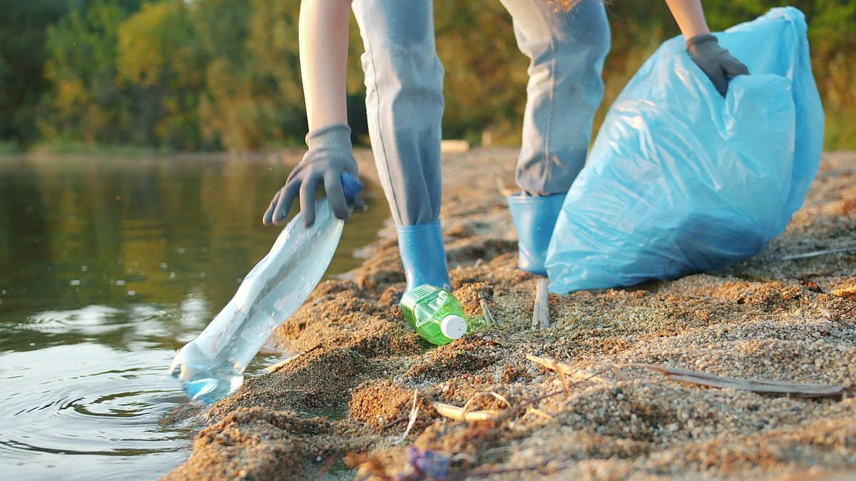 Eine Person sammelt an einem Fluss Müll ein
