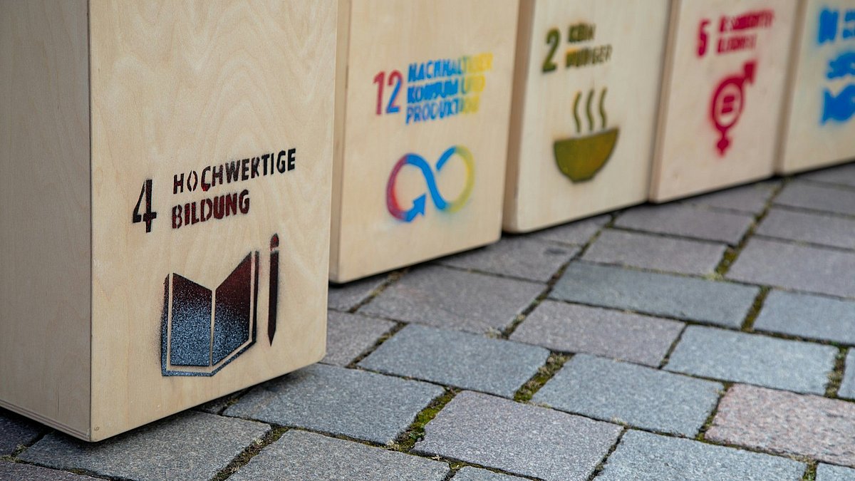 Holzaufsteller mit aufgedruckten SDGs stehen auf dem Boden