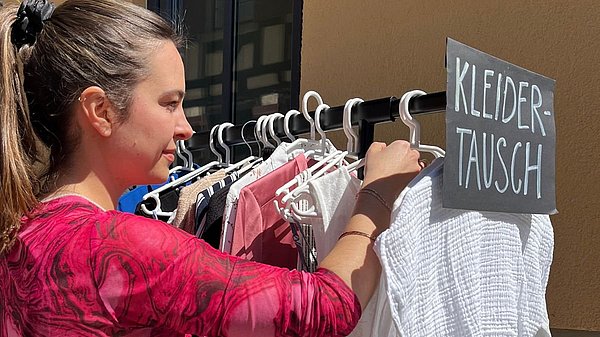 kleidertauschparty-schwäbisch hall Junge Frau sucht bei Kleidertauschparty an einer Kleiderstange nach Kleidungsstücken.