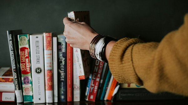 Eine Hand greift in ein Bücherregal