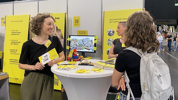 Zwei Personen stehen auf einer Berufsmesse an einem Stehtisch und unterhalten sich