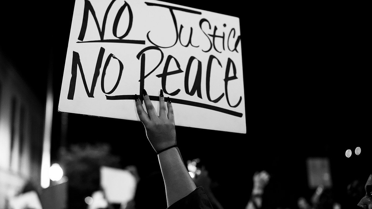 Eine Person hält auf einer Demo ein Schild mit der Aufschrift "No Justice No Peace" hoch