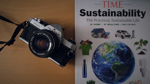 Eine Kamera liegt neben einer Zeitschrift, die die Überschrift "Sustainability" trägt