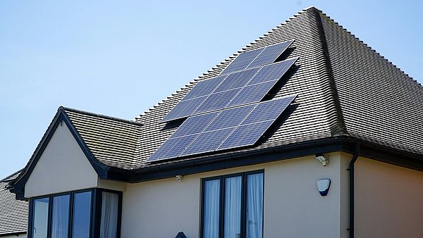 Hausdach mit installierter Photovoltaikanlage aus mehreren Solarmodulen, die auf der sonnigen Dachfläche Strom aus Sonnenenergie erzeugen.
