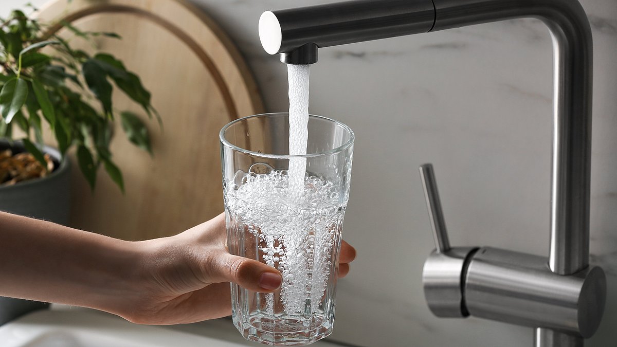 Wasser Marsch Eine Person hält ein Glas unter den laufenden Wasserhahn.