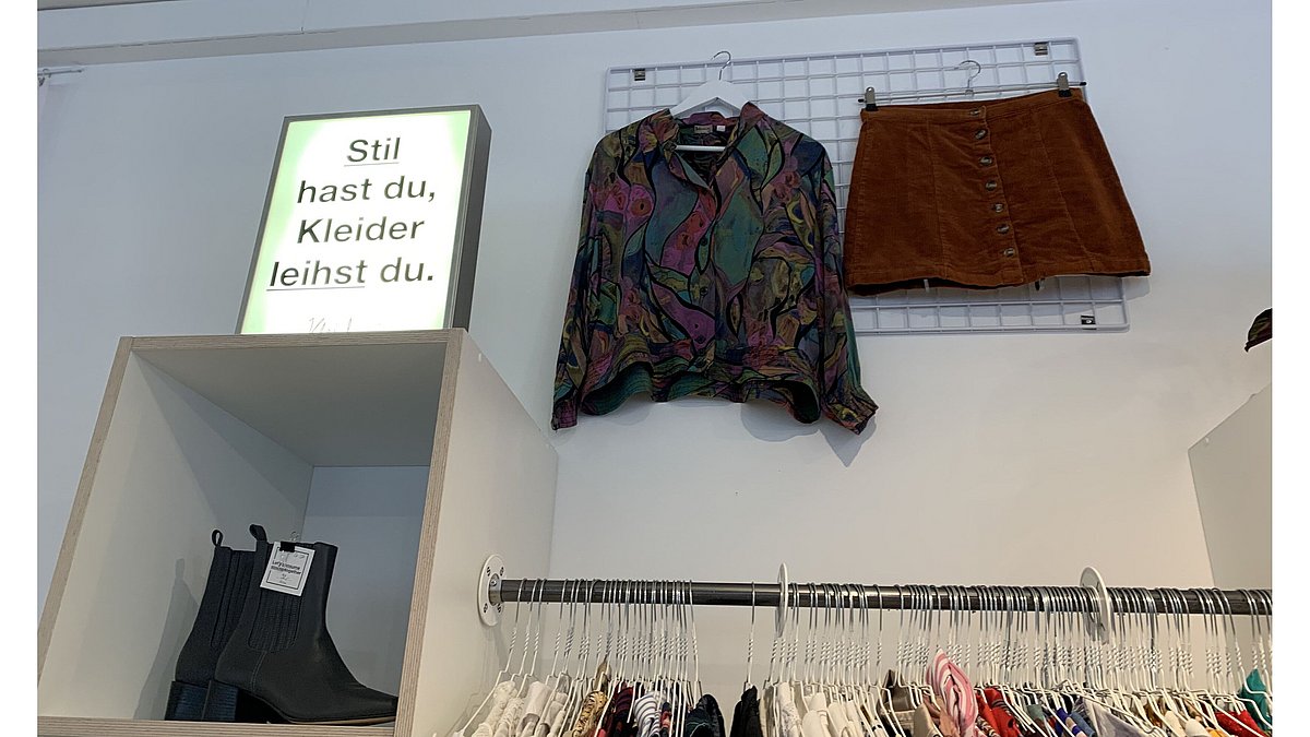 Stil hast du, Kleider leihst du. In der Kleiderei steht auf einem Regal eine Leuchtreklame mit dem Text: Stil hast du, Kleider leihst du.